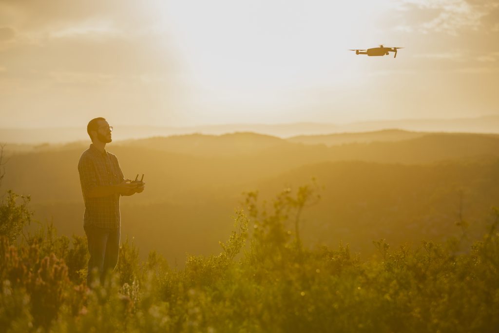 Drone despegando de la mano de un piloto al atardecer, con los colores del cielo crepuscular de fondo, simbolizando el inicio de una aventura aérea en España.